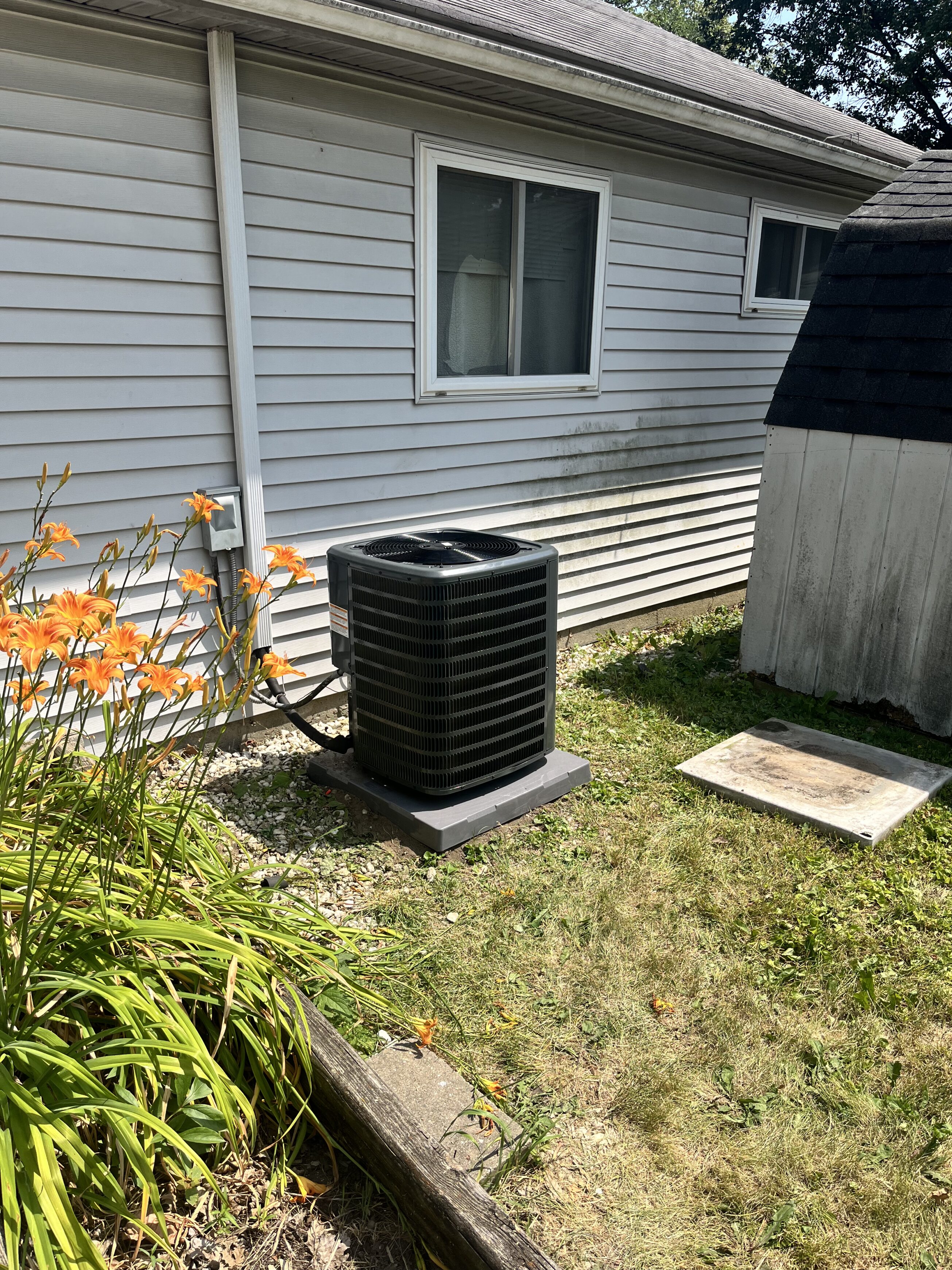 Outside air conditioner unit of a home with flowers and bright green grass on a sunny day